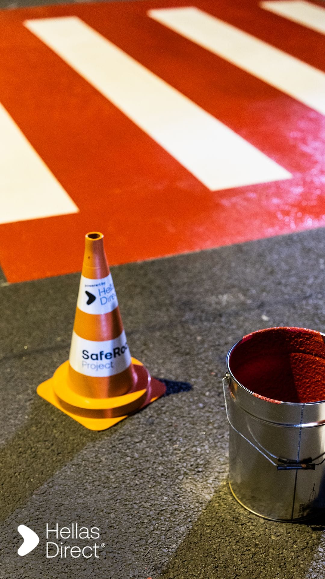 A branded safe roads project road safety cone in front of a crosswalk 