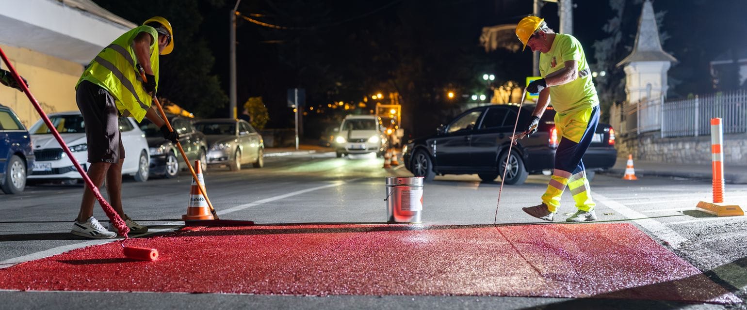 Two men of the Safe Roads Project crew paint a crosswalk outside a school during the night