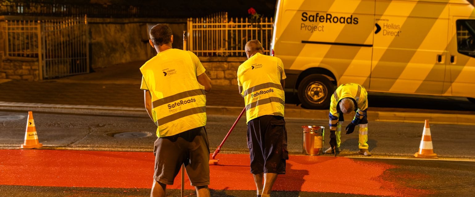 Three men of the Safe Roads Project crew paint a crosswalk outside a school, the Safe Roads project van in the background